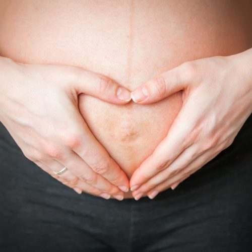 close-up pregnant woman holding her hands in a heart shape on her belly