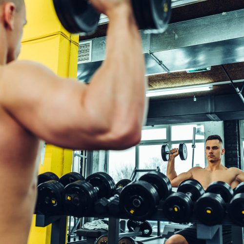 Cropped shot of a young muscular man lifting dumbbells at a gym